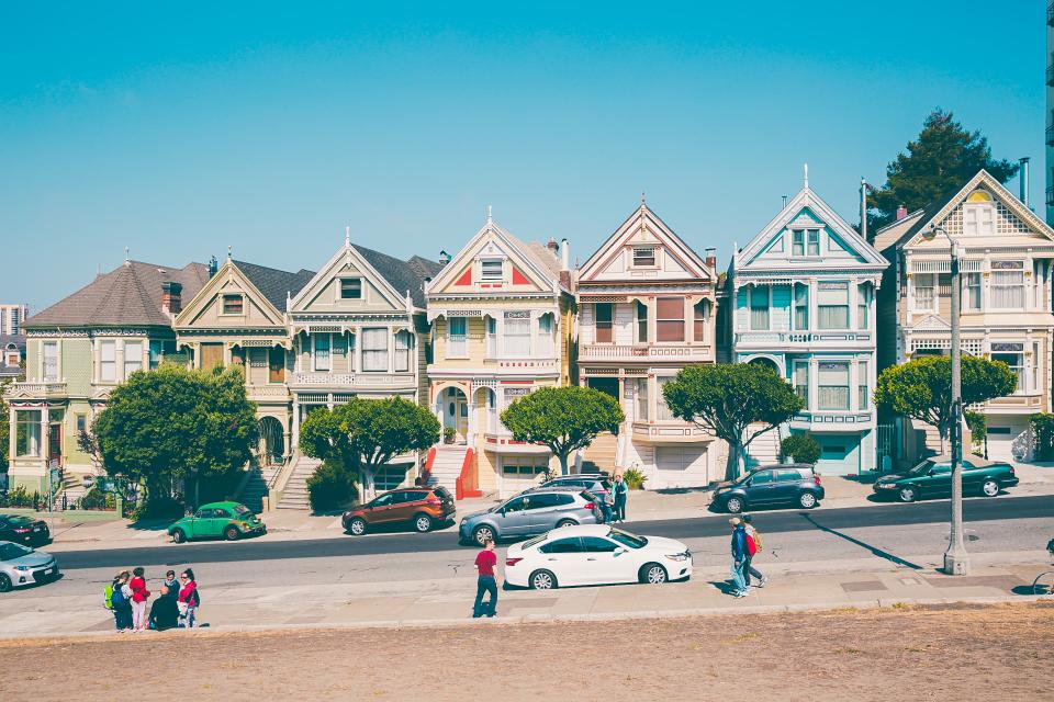 A row of colourful houses along a neighbourhood street with people walking by