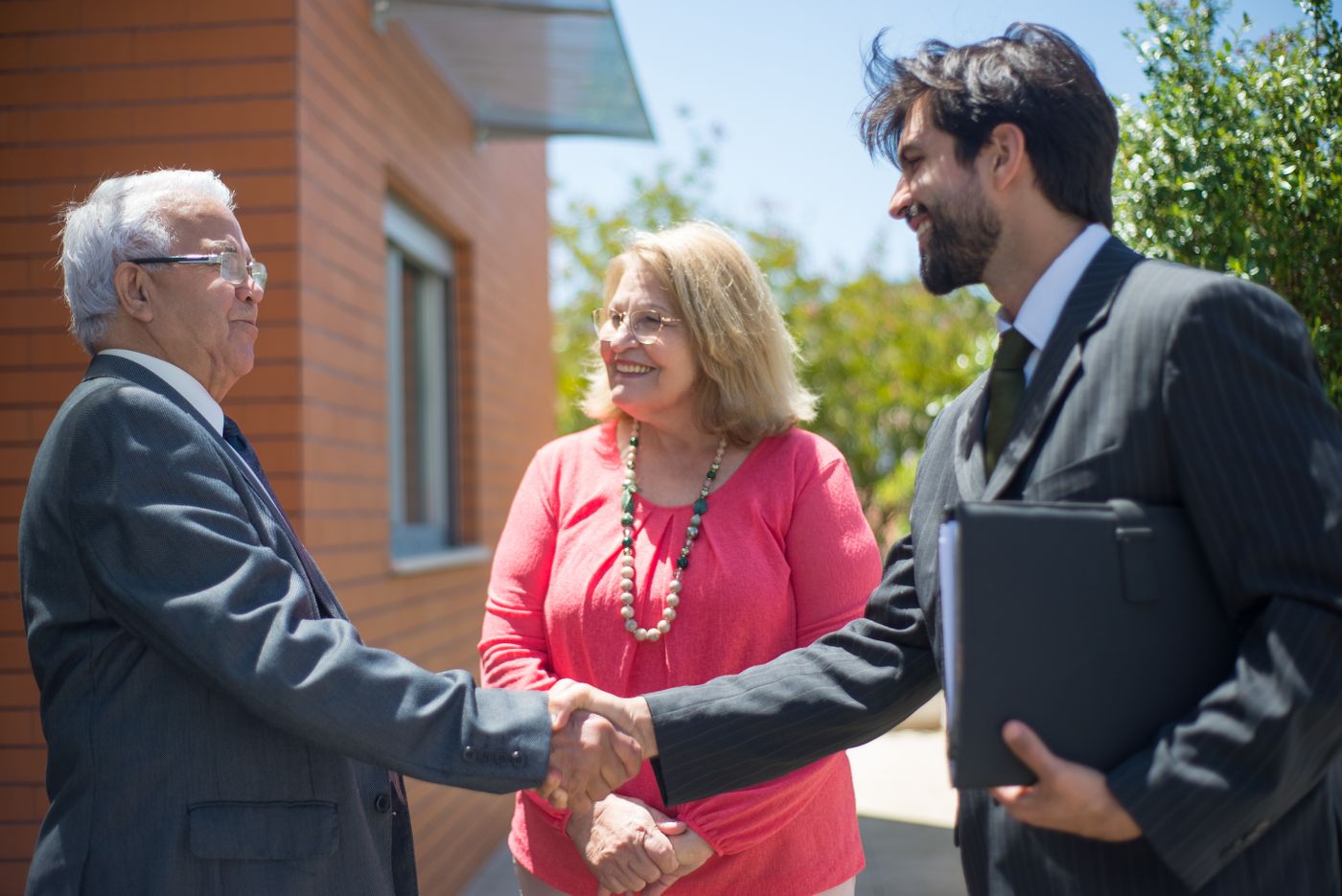 A couple shaking hands with an agent outside their home