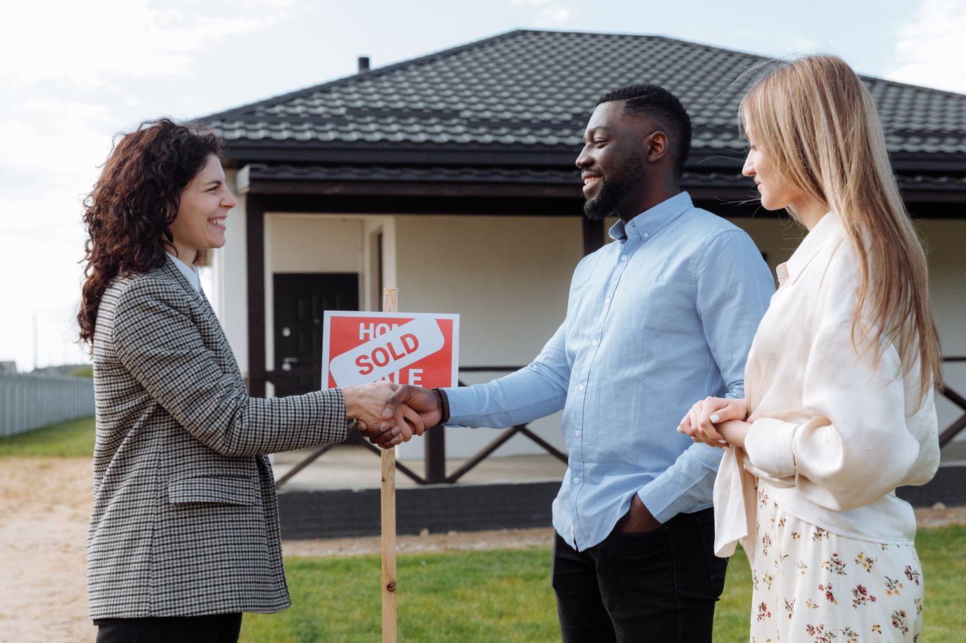 An agent shaking hands with a couple in front of their sold home