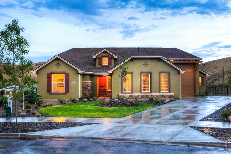 A single-storey family home with the front door open and lights on inside